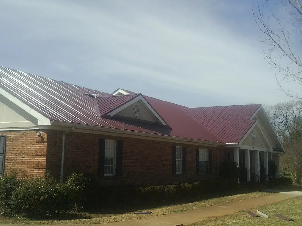 Red metal roof with gabled entries on a long brick building, from a Hail Damage Roof Repair job in Beckley