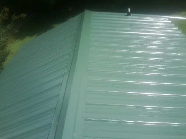 New green metal panels meeting at the ridge of a roof — Flat Roof Repair work by our crew in Beckley