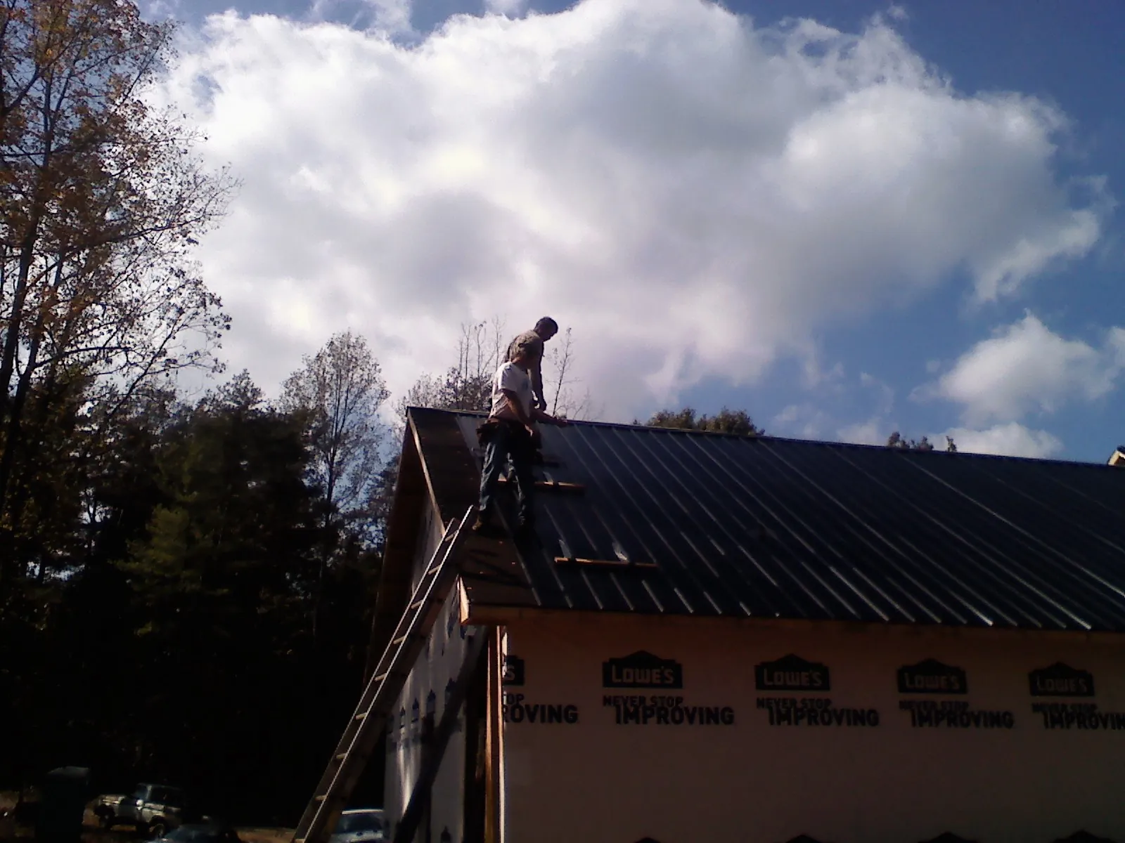 Roofer fastening dark metal panels high against a cloudy sky, from a Roof Inspection job in Beckley